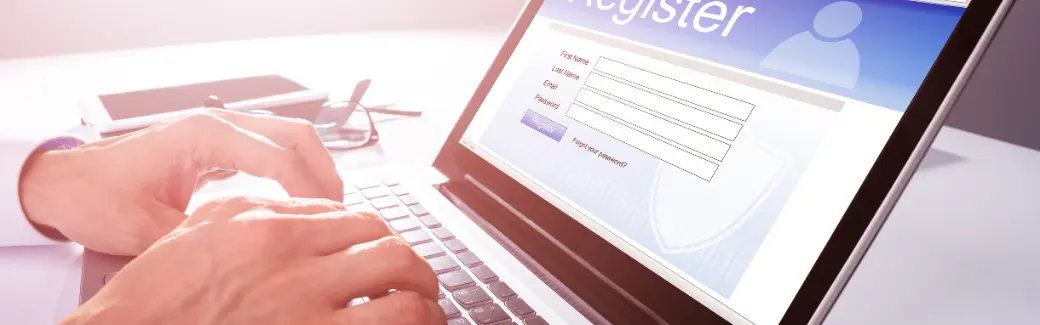 mains sur un clavier d'ordinateur portable dont l'écran affiche un formulaire d'inscription