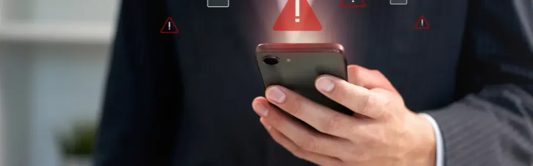 personne en costume tenant un smartphone au-dessus duquel s'affichent des icônes d'alerte rouges