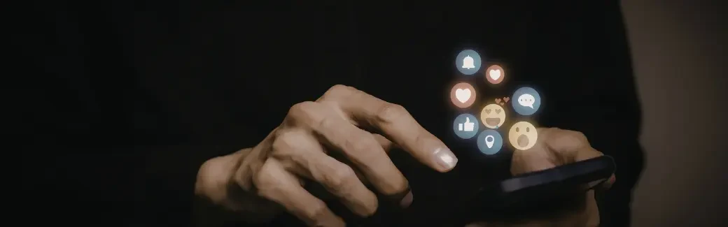 mains sur un smartphone dans la pénombre avec des icônes de réseaux sociaux flottantes