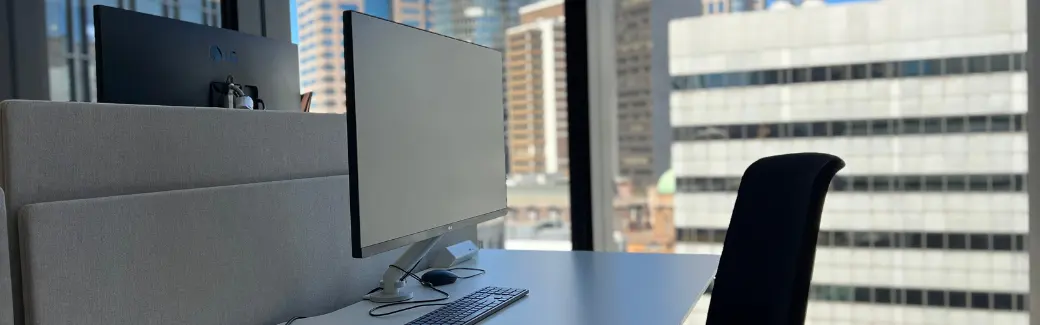 bureau vide avec écran d'ordinateur et fauteuil devant une fenêtre donnant sur des immeubles