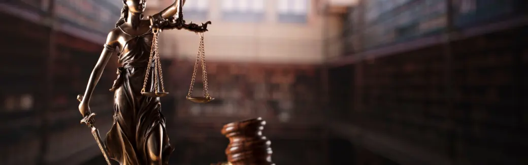 statuette de la justice tenant une balance et une épée devant un marteau de juge, dans une bibliothèque de droit