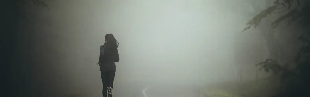 silhouette d'une personne vue de dos qui s'éloigne en courant sur une route dans un épais brouillard